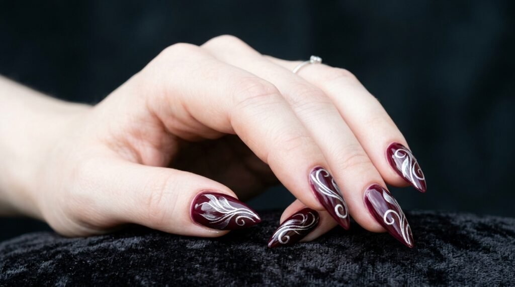 Abstract silver floral swirl lines on dark wine stiletto nails on very white skin.