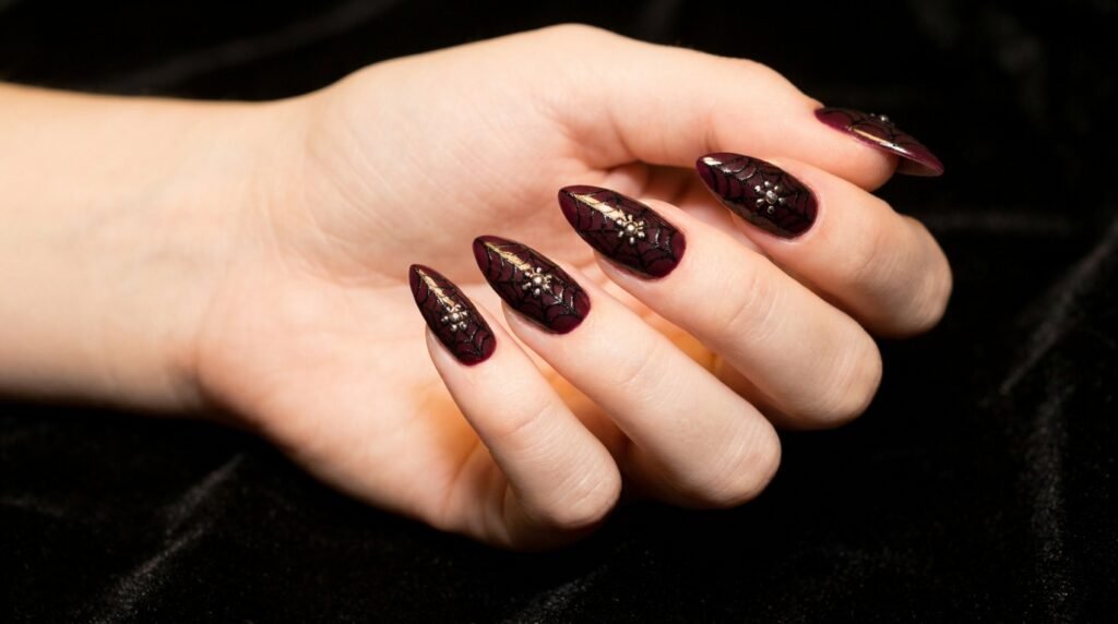 Black lace patterns with silver floral centers on burgundy stiletto nails on very white skin.
