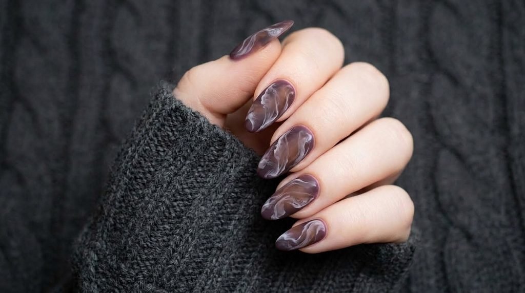 Close-up view of an 18-year-old female hand with white skin showing matte plum and brown marble swirl nails.