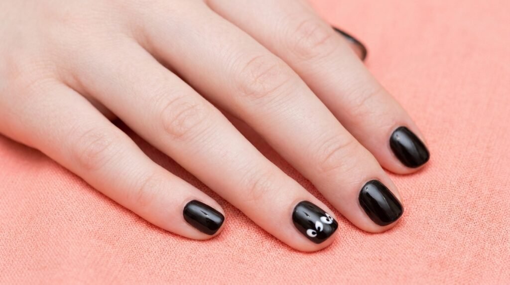 Short round nails on a white skin 18-year-old hand with black French tips and a tiny ghost face detail.