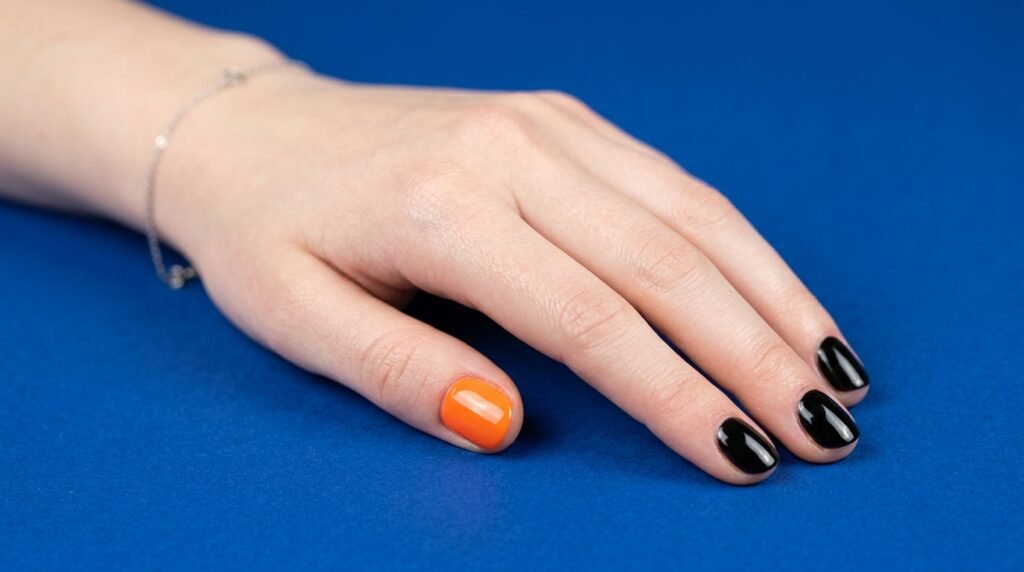 Short round nails on an 18-year-old white hand painted black with one orange accent nail on a blue background.