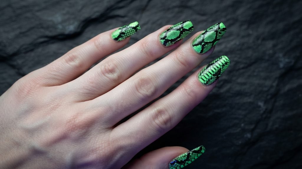 Coffin nails showing black snakeskin patterns over glowing green underlay on dark slate.