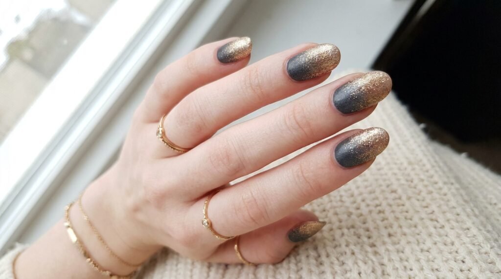 Oval nails with dark charcoal polish transitioning smoothly into warm gold micro-glitter.