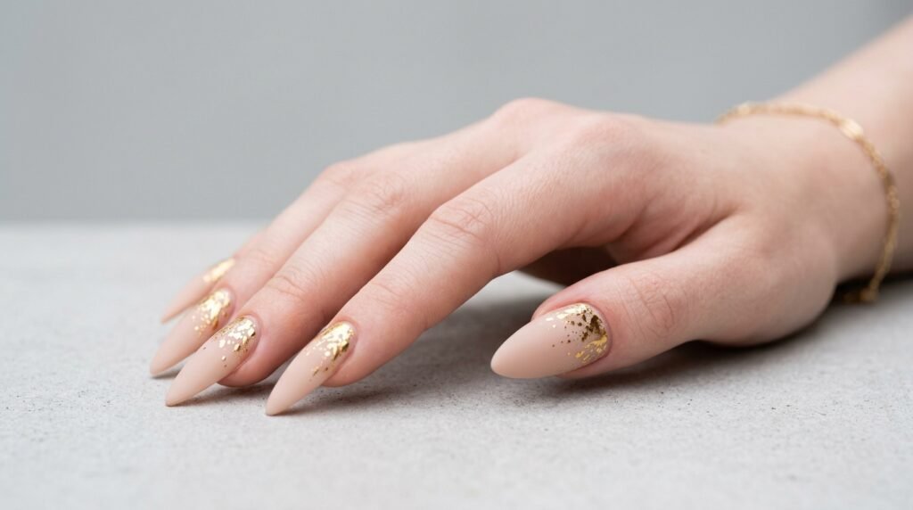 An 18-year-old female hand with very white skin showing long almond nails with gold splatter at the cuticles.