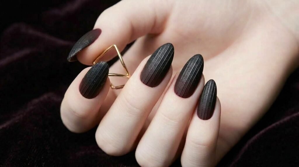 Close-up of matte black to burgundy ombré nails with fine black glitter shimmer on a white female hand (18), soft moody light.