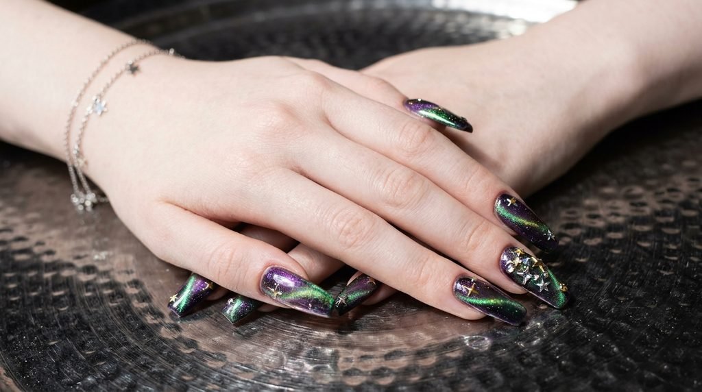 Long coffin galaxy nails on an eighteen-year-old female hand with very white skin against a dark silver background.