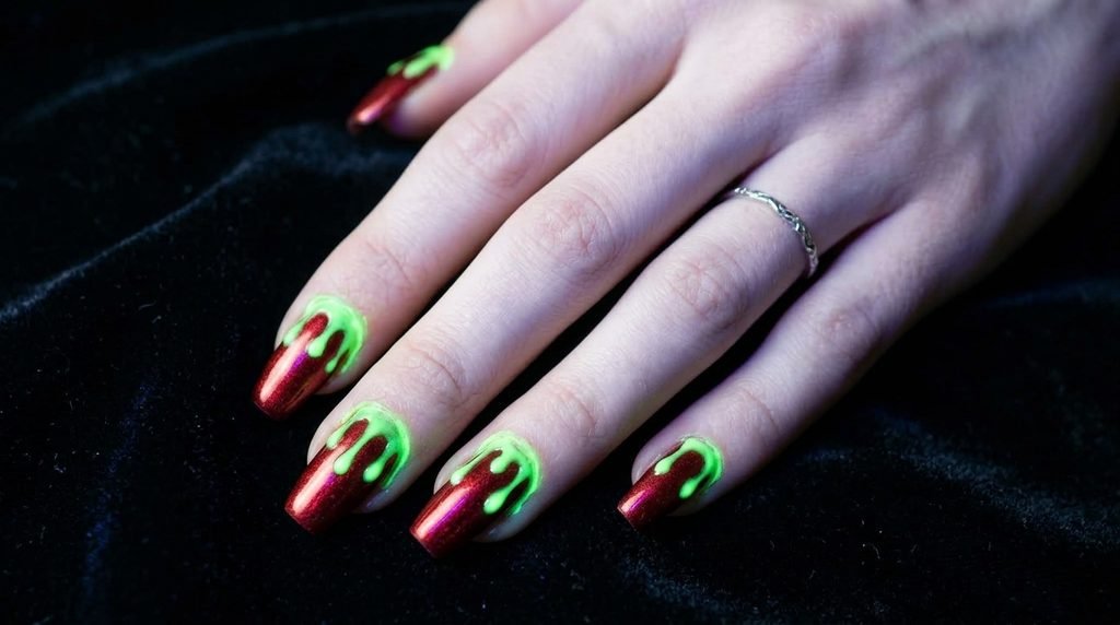 Metallic red coffin nails featuring thick glowing green drips from cuticles on dark velvet.