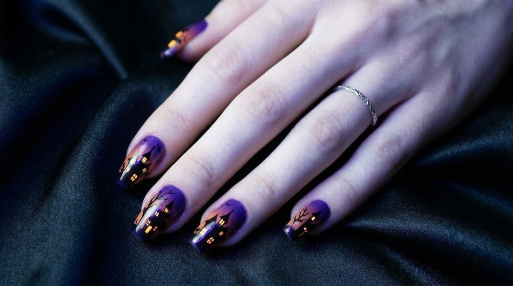 Long coffin nails with purple-orange gradient, black haunted house silhouettes, and glowing yellow windows.