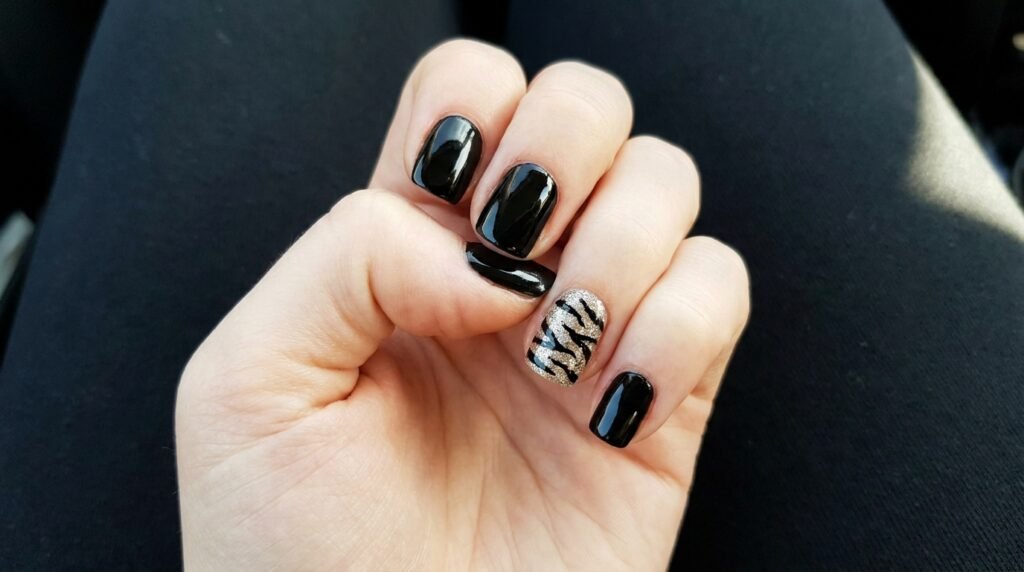 Female hand displaying glossy black nails with a gold glitter tiger stripe accent nail design.