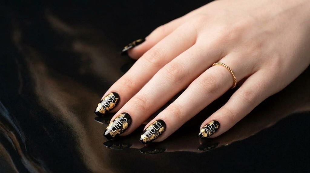 Black coffin nails decorated with gold foil specks and white text on a fair female hand.