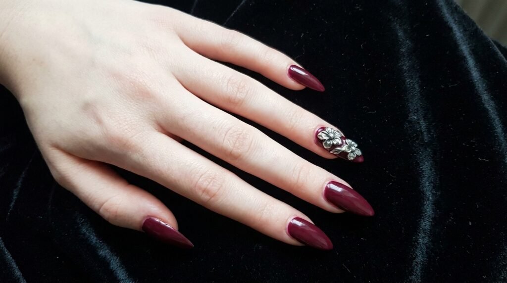 Raised 3D silver acrylic flower art on deep wine stiletto nails on very white skin.
