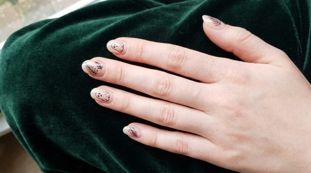 Short oval nude nails with minimalist black outline ghosts and fern fronds on white skin.