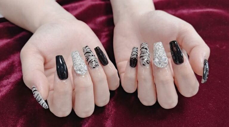 Close-up of an 18-year-old female hand with white skin showing glossy black almond nails with gold glitter ombré tips.