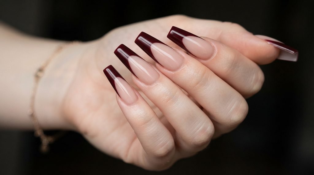 A low-angle detailed photograph of long coffin nails with a substantial oxblood French manicure