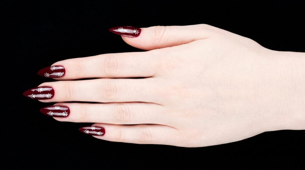 Micro silver daisy art painted on oxblood red stiletto nails on very white skin.