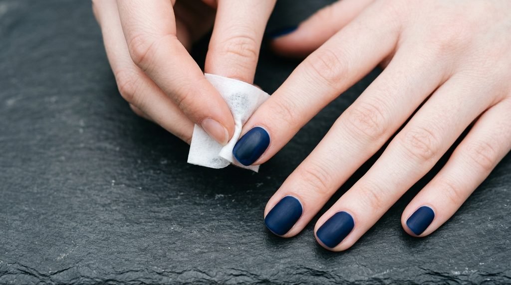 Alcohol wipe refreshing a matte gel nail on an 18-year-old female hand with very white skin.