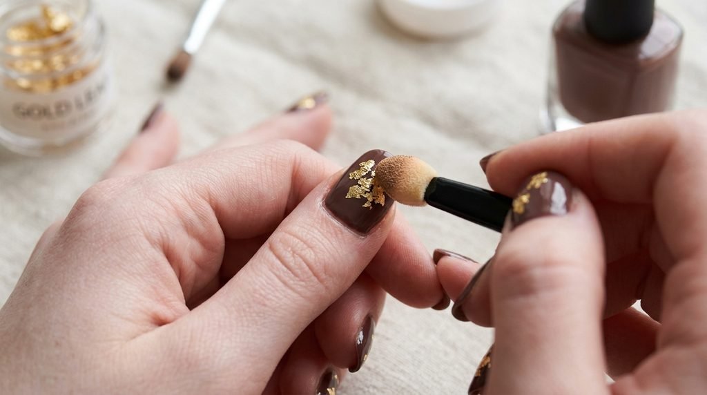 Applying gold leaf to regular mocha polish with a foam tool on fair skin.