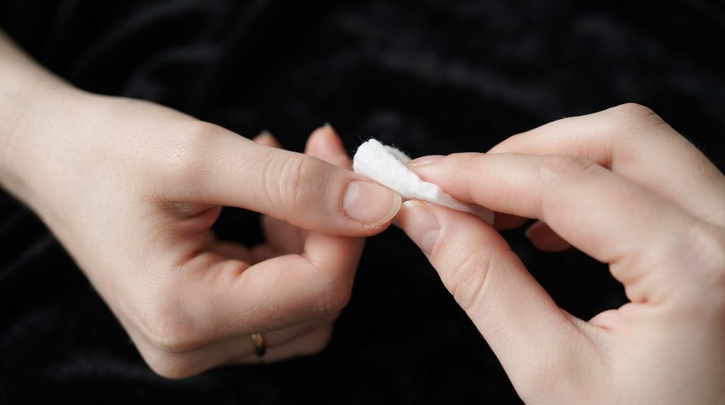 A lint-free wipe cleansing a natural nail surface on an 18-year-old female hand with very white skin.