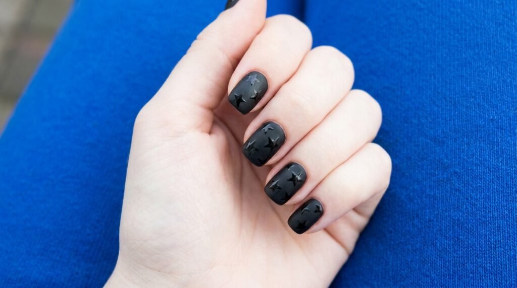 Matte black short nails on an 18-year-old white hand with glossy black stars painted on the surface.