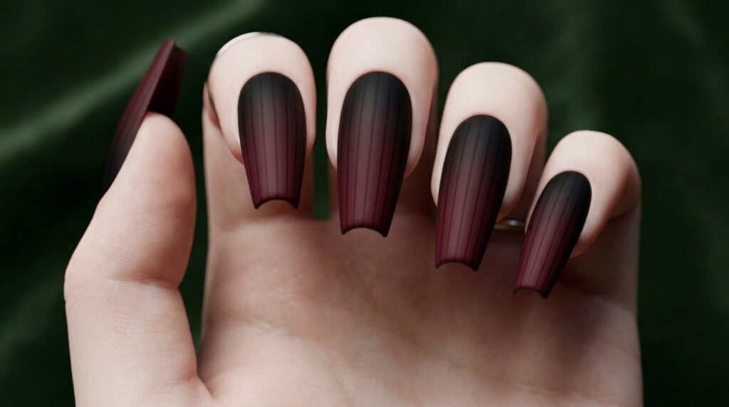 Low-angle close-up of dramatic matte black to burgundy ombré coffin nails on a white female hand (18), blurred urban dusk background.