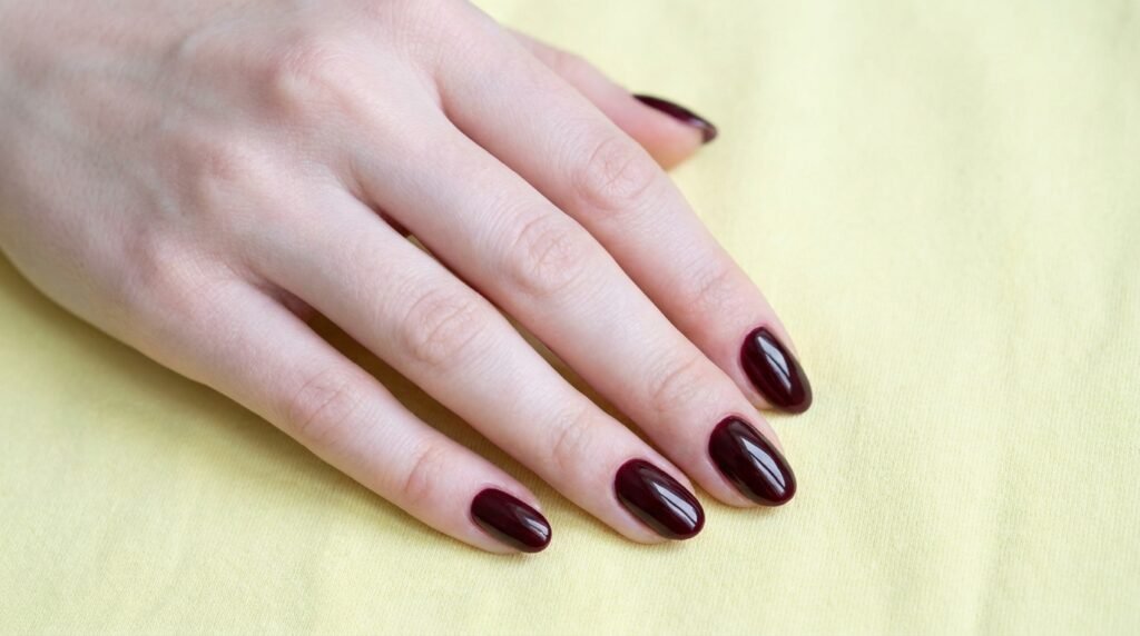 Medium oval nails on a white skin female hand painted in glossy dark cherry burgundy polish.