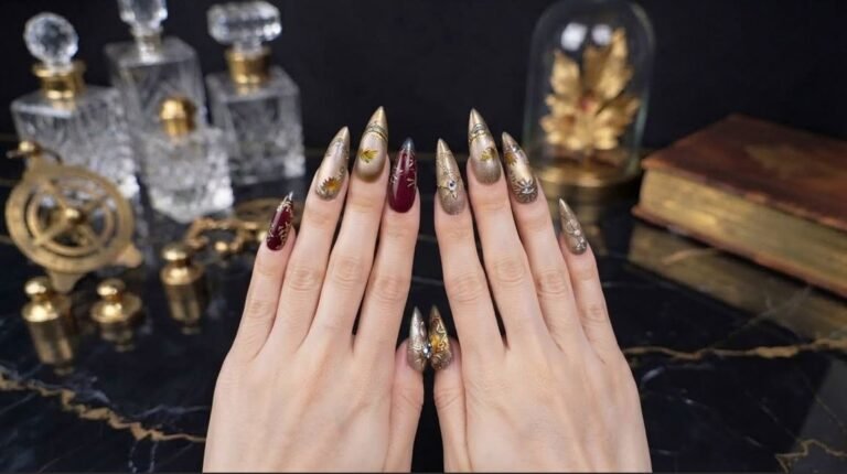 A close-up of a woman's hand with almond nails featuring deep burgundy, gold chrome, and a tiny ghost.