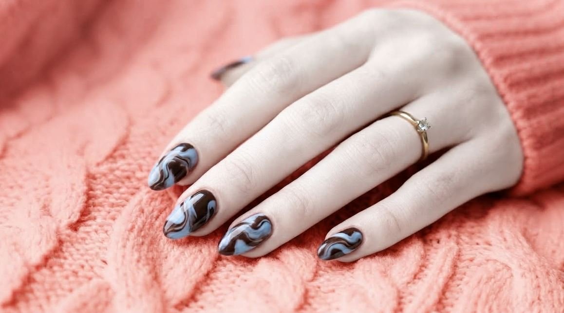 Close-up of an 18-year-old female hand with white skin showing glossy dark chocolate and sky-blue almond nails.