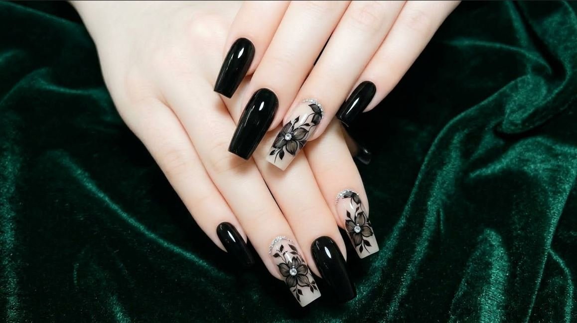 Close-up of a female hand with smooth white skin showing coffin nails with black floral art over a nude base.