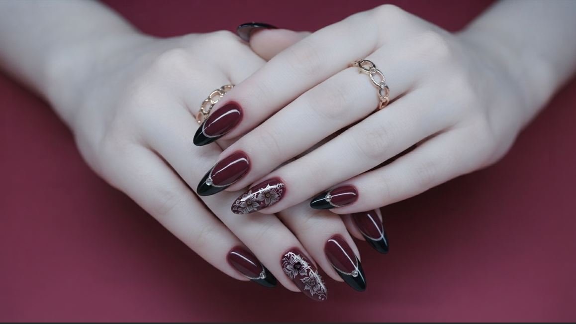 Close-up of an 18-year-old female hand with very white skin showing burgundy and black stiletto nails with silver floral designs.
