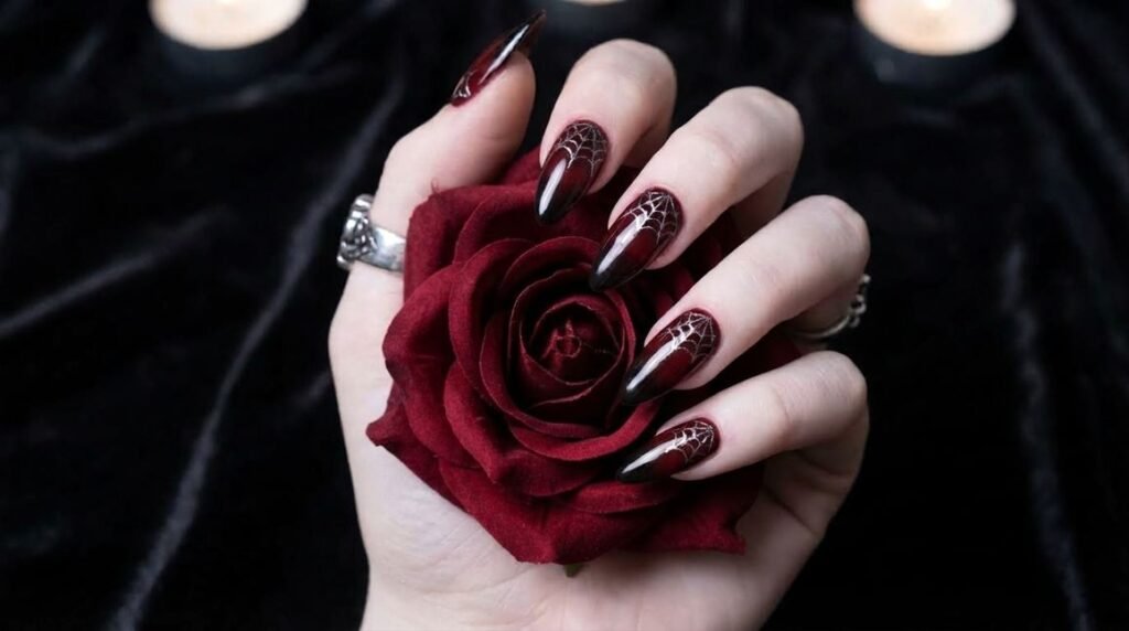 Oxblood red to black ombre almond nails with silver spiderwebs on very white female hand.