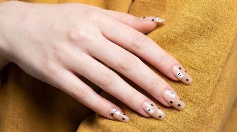 Close up of an 18-year-old female hand with white skin showing short nude nails decorated with tiny white ghosts.