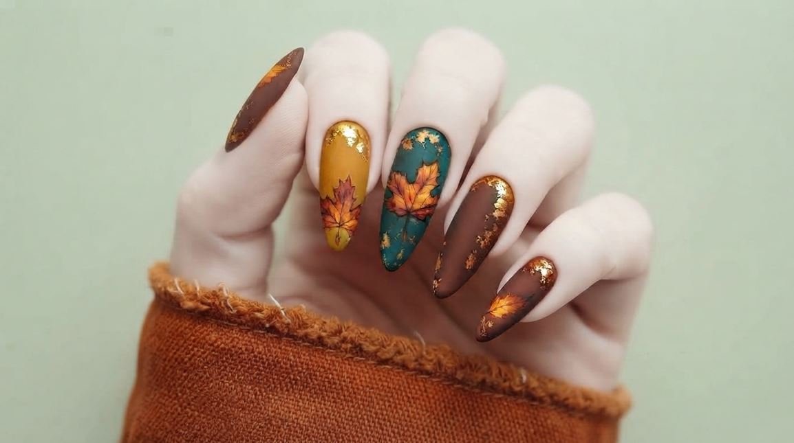 Complete female hand with very white skin showing all 5 mismatched autumn nails with maple leaf art.