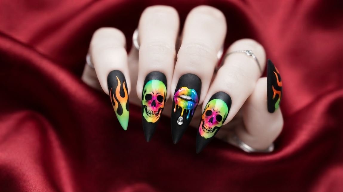 Close-up of 18 year old female hand with very white skin showing long stiletto nails with neon skull artwork on matte black polish.