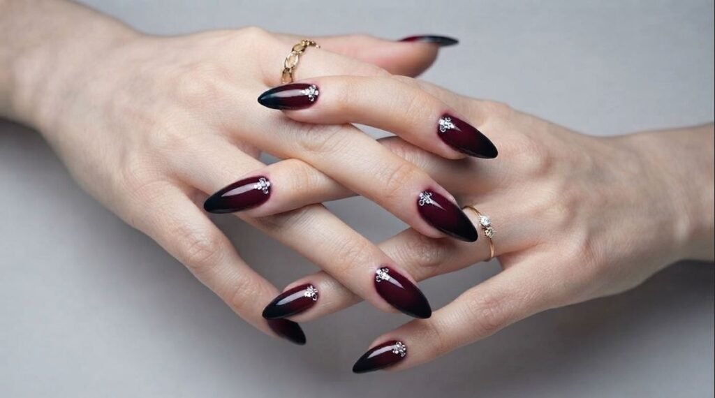 Small silver rhinestone flowers placed near cuticles on dark stiletto nails on very white skin.