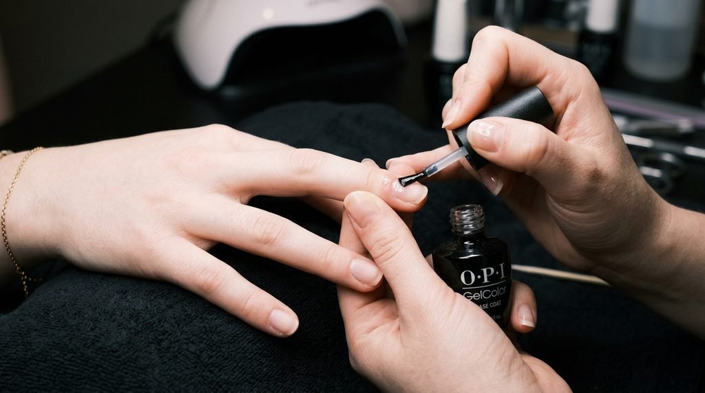Clean prepped natural nails on female hand receiving gel base coat application.