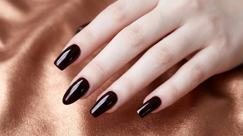 Four nail shape extensions painted in deep black cherry gel resting against a copper metallic backdrop.