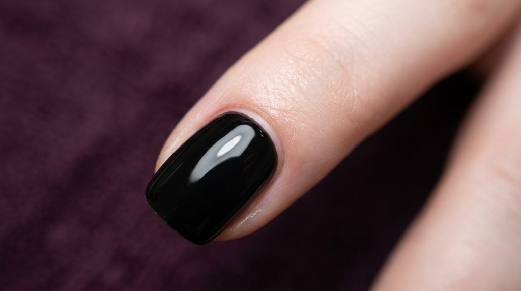 Macro photograph showing a precise gap between jet black polish and cuticle on a pale female nail.