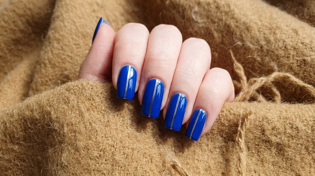 Cobalt blue square nails with silver metallic stripe art on very white skin.