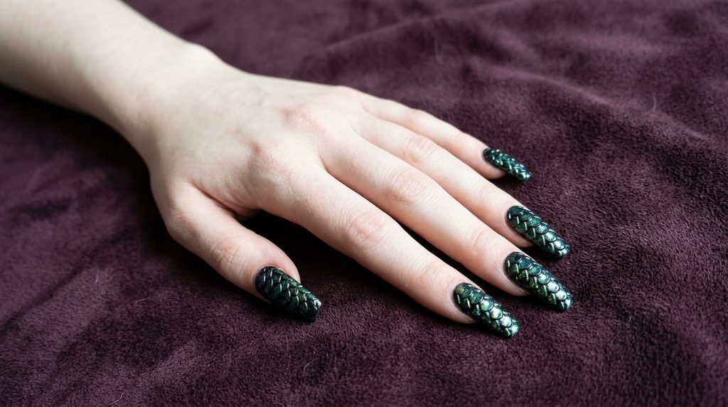 Long coffin nails with snake scale art on a pale female hand over dark plum suede.