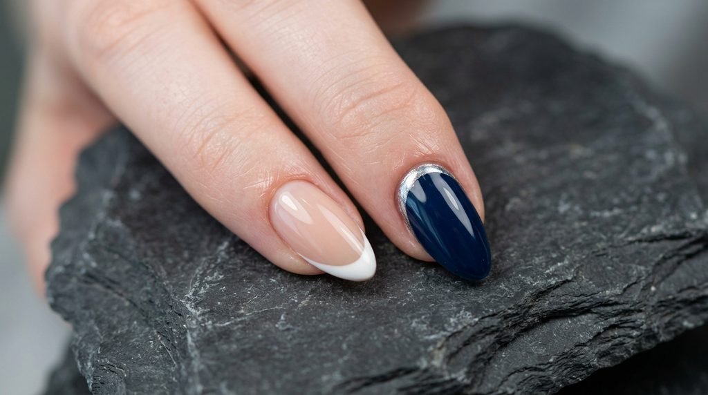 Close-up showing two almond nails: one with a classic white French tip, and the next with a modern reverse silver chrome cuticle line against blue polish.