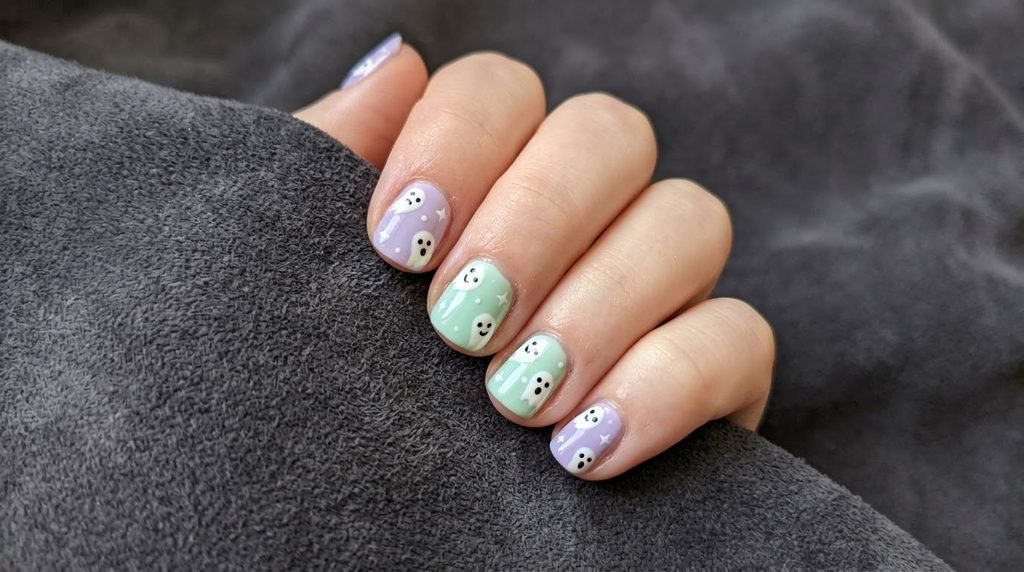 Pastel Halloween ghost nails on an 18-year-old hand over charcoal grey suede.