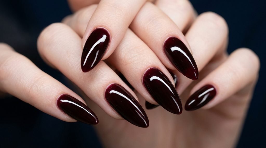 Long almond nails featuring a plump glass gel top coat over black cherry polish on a midnight blue backdrop.