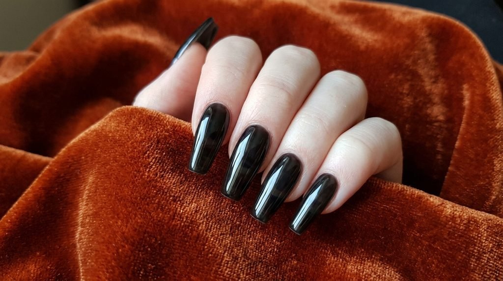 Coffin black glass nails on an 18-year-old female hand with very white skin against burnt orange velvet.