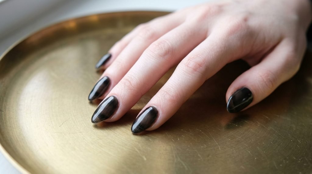Close-up of an 18-year-old female hand with very white skin featuring sheer black jelly nails over a brass plate.