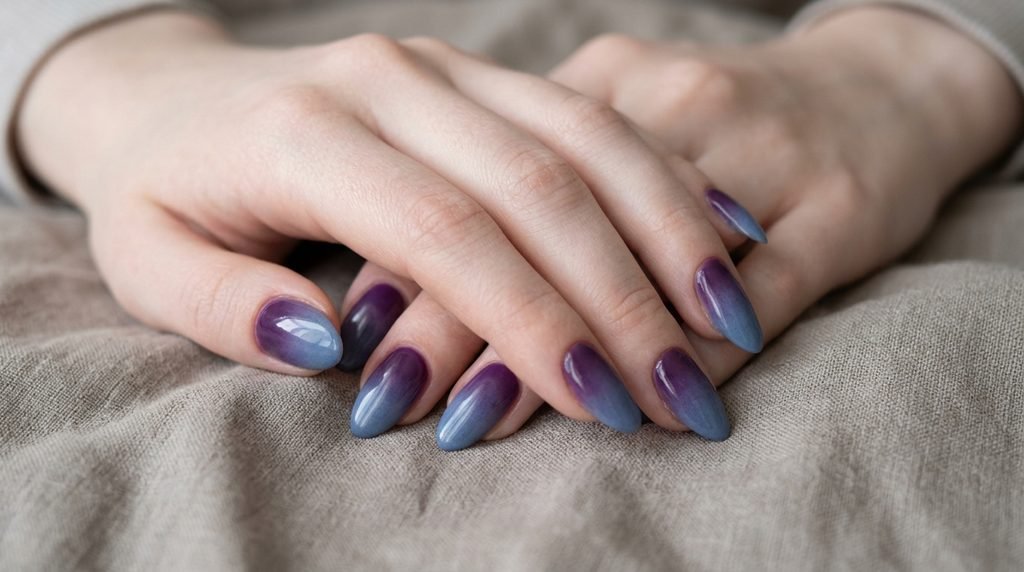 Almond nails painted in purple and blue gradient against neutral taupe linen.