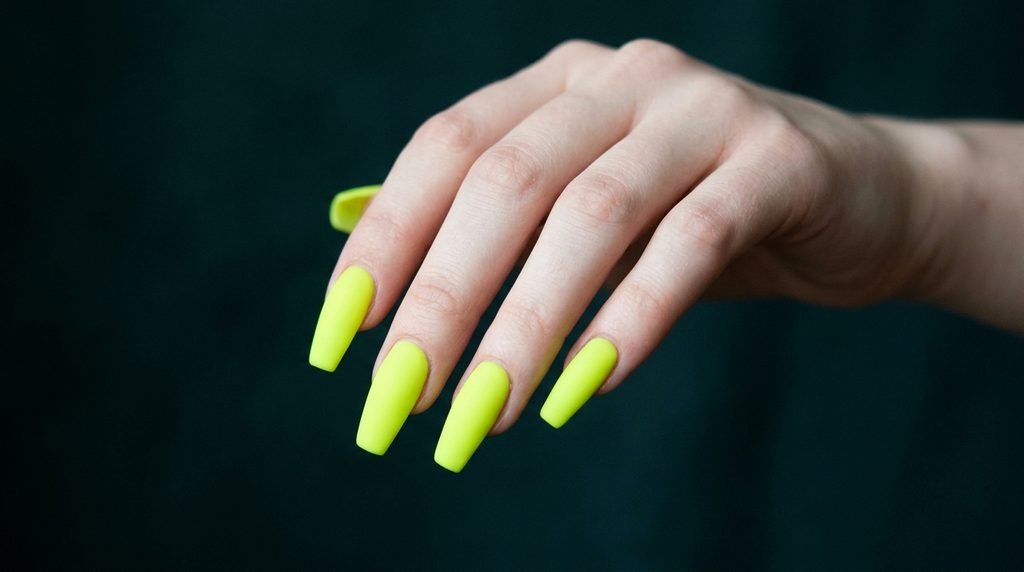 Angle shot of an 18-year-old hand with very white skin displaying tapered neon green coffin nails over dark teal fabric.