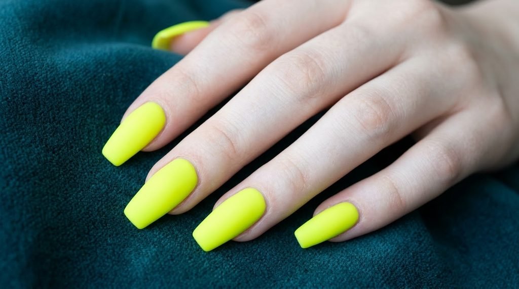 Macro photograph of clean cuticle lines on matte neon chartreuse coffin nails worn by an 18-year-old with very white skin.