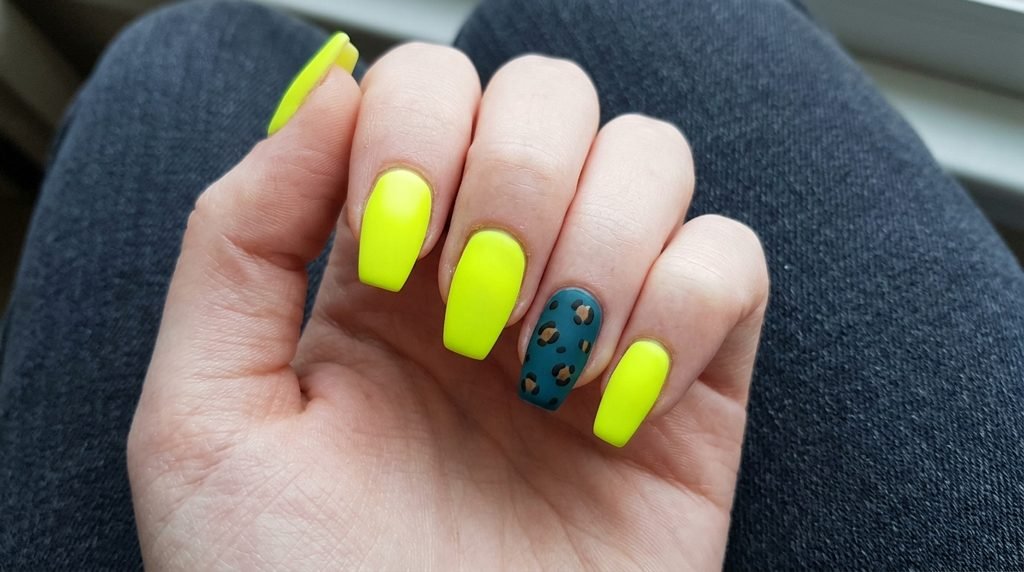 Short coffin nails painted in matte neon chartreuse on an 18-year-old hand with very white skin against dark teal background.