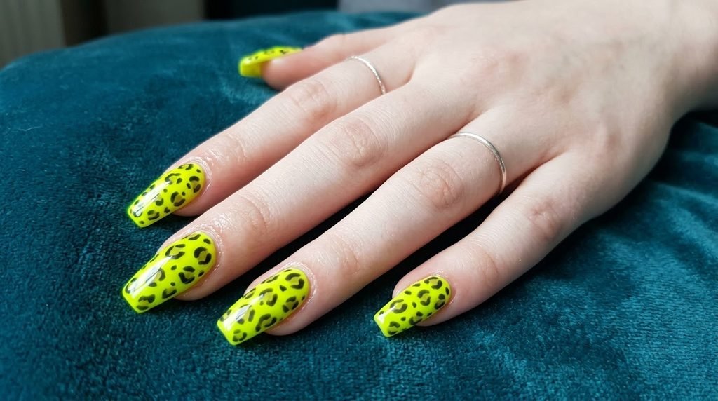 Completed salon set of neon chartreuse and leopard coffin nails on an 18-year-old female hand with very white skin.