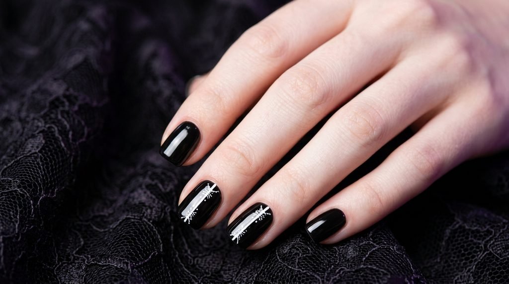 Focused close-up of two short square nails on an 18-year-old female hand with smooth white skin, painted with glossy black and featuring simple vertical white bone lines with small cross segments representing joints, against a dark black lace background with hints of violet.